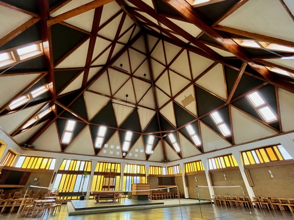 The interior of the pyramid. The roof comes to a point off centre, and is made of geometric shapes with white and black triangles. Around the walls of the room, and at the lower third of the image, are vertical windows which have yellow panes of glass.