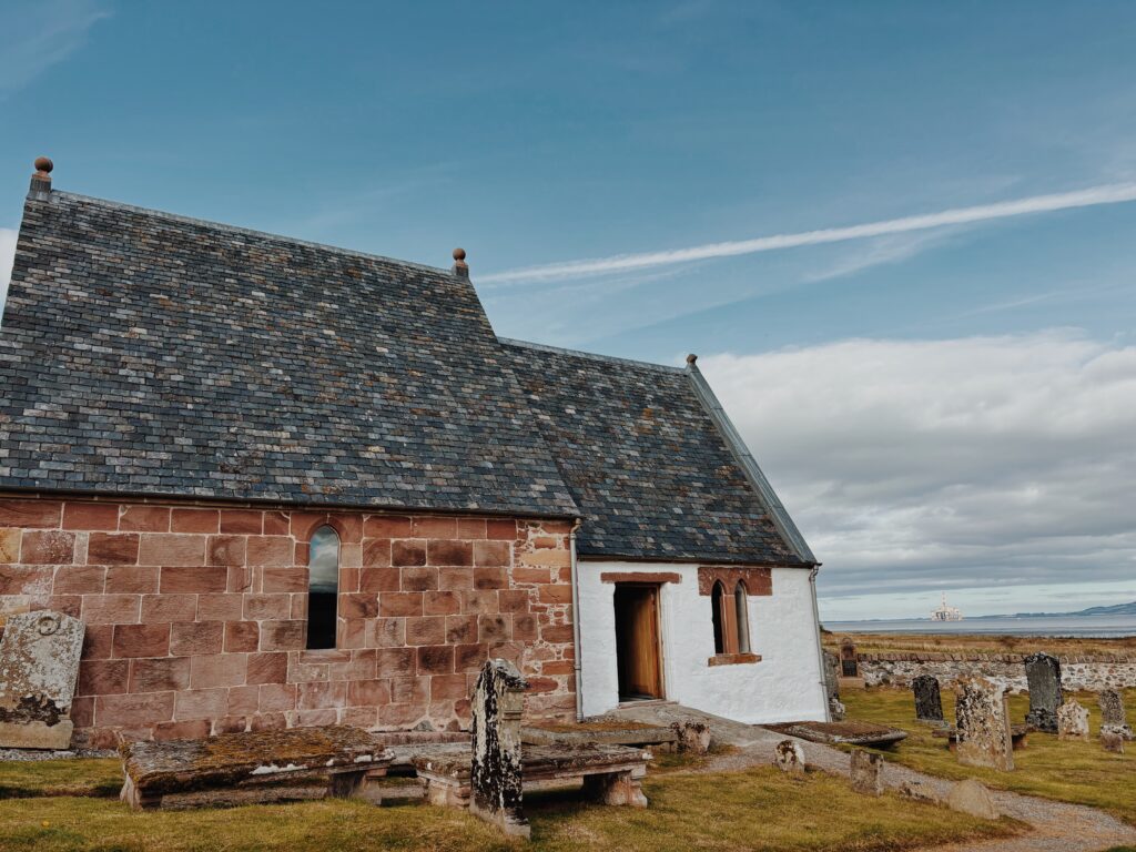 Kirkmichael church which has two faces to the building - on the left is red sandstone brick and on the right white limewash, both with slate roofs. Surrounding the church is a graveyard