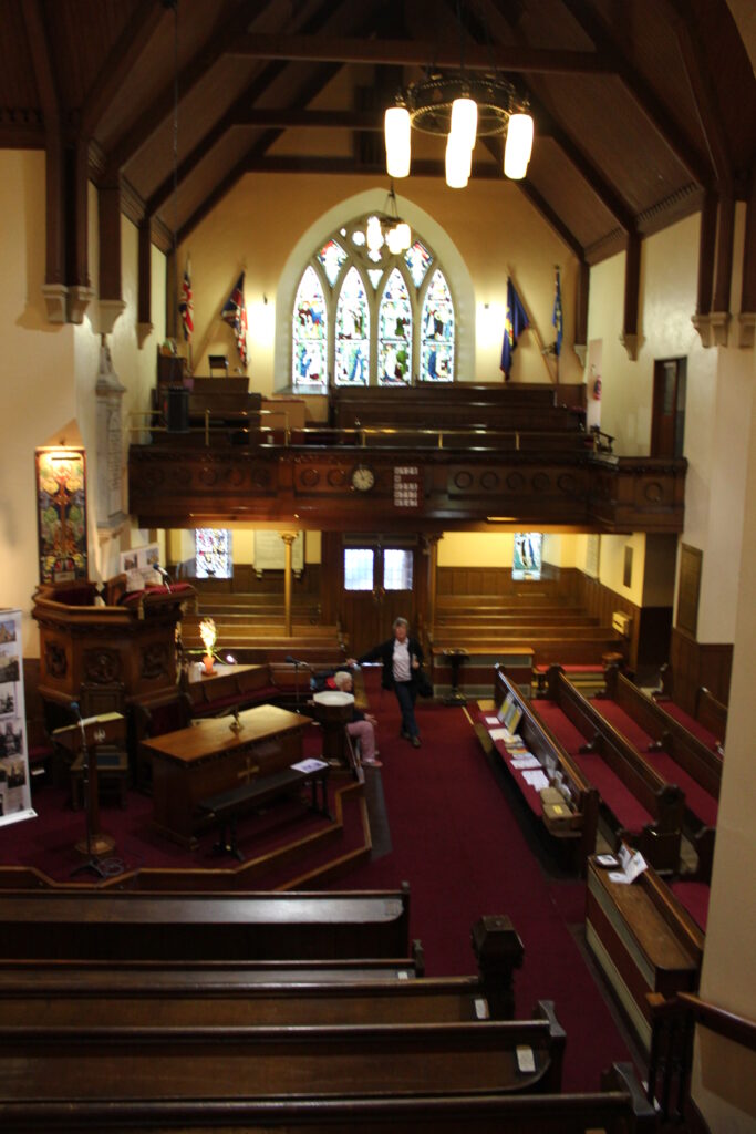 Colour photograph of interior of church with pews, pulpit and stained glass window
