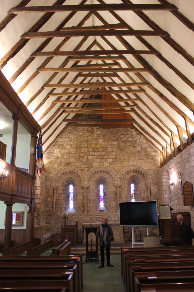 Colour photo of interior of church from aisle with stone walls and wooden beams at the roof