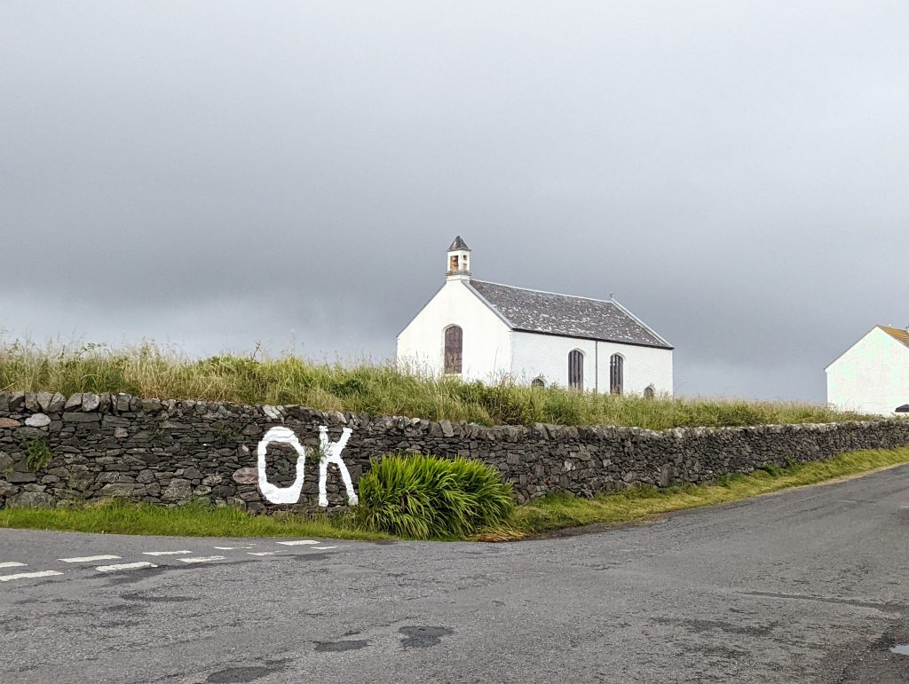 View of the church from the corner of the road with 'OK' painted on the drystone wall