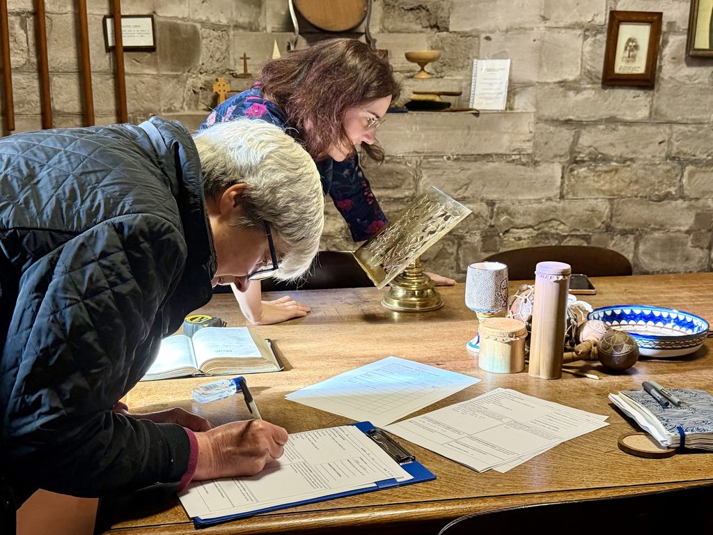 Two volunteers in the vestry, one filling in a recording sheet and the other inspecting a lectern