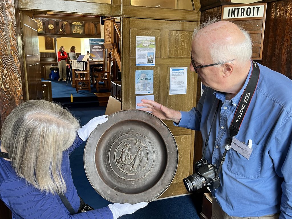 Two volunteers holding an alm dish with white gloves on